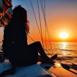 A girl is sitting on the deck of Caliu sailboat watching the sunset in hour full day tour with sunset