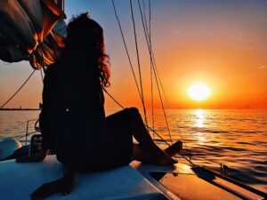 A girl is sitting on the deck of Caliu sailboat watching the sunset in hour full day tour with sunset