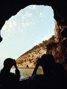 Two girls are taking a picture visiting a cave in es caló, Formentera in our full day sailing tour, discovering the best places in Formentera