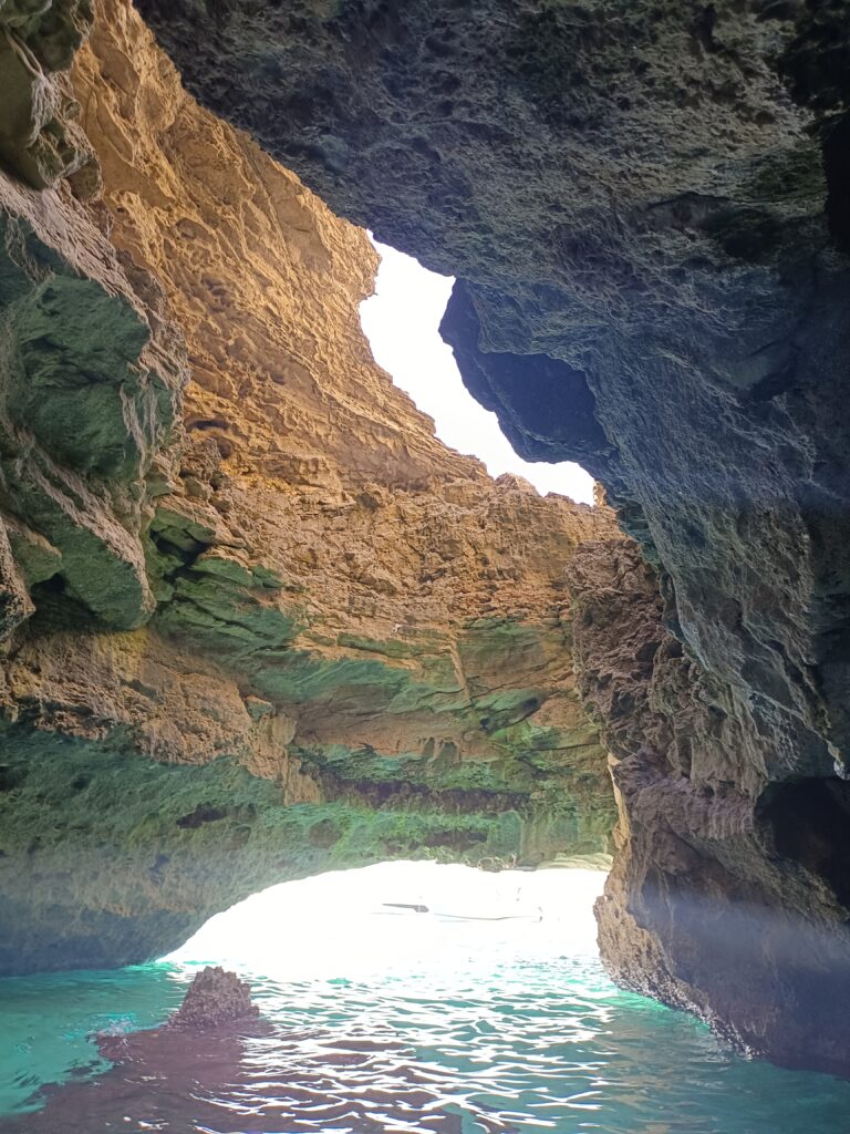 A serene view inside a cave at Cala Saona, with sunlight filtering through the opening and reflecting on the clear waters, highlighting the unique places explored on our tours.