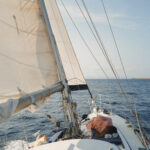 Caliu on sails. Two girls are lying and relaxing enjoying the calm of the navigation in our half day tour