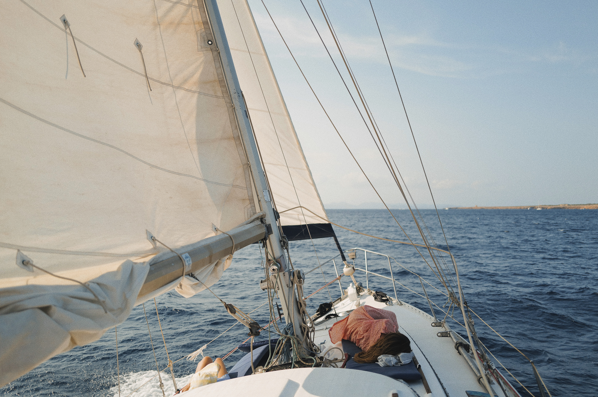 Caliu on sails. Two girls are lying and relaxing enjoying the calm of the navigation in our half day tour