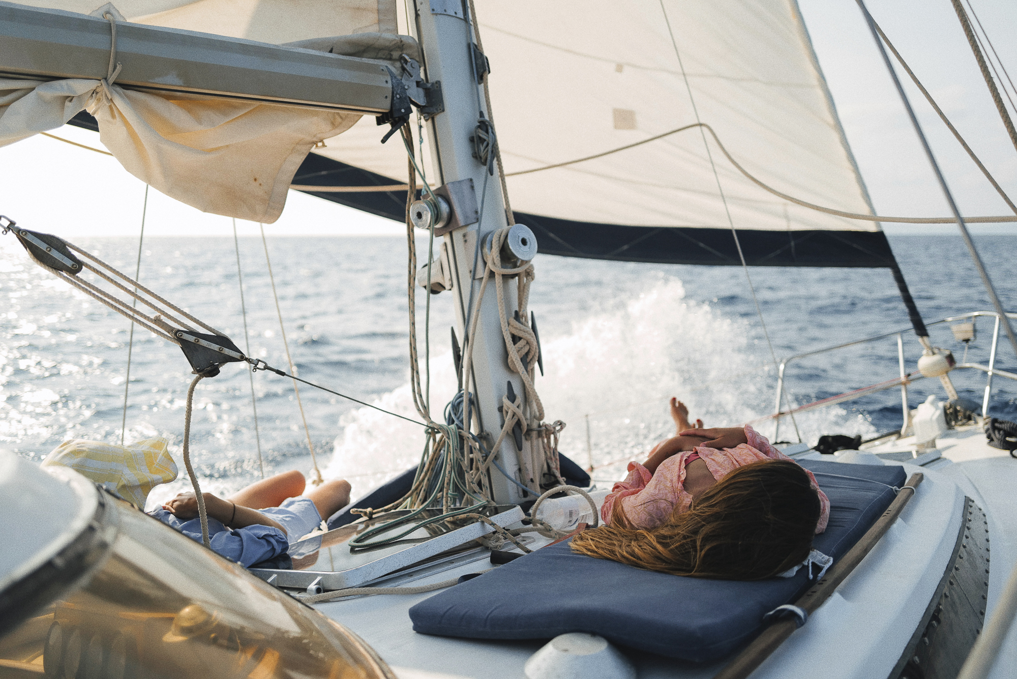 Passengers lounging on 'CALIU' deck, sailing with full sails on a breezy Formentera day, showcasing the yacht's comfort and stability.