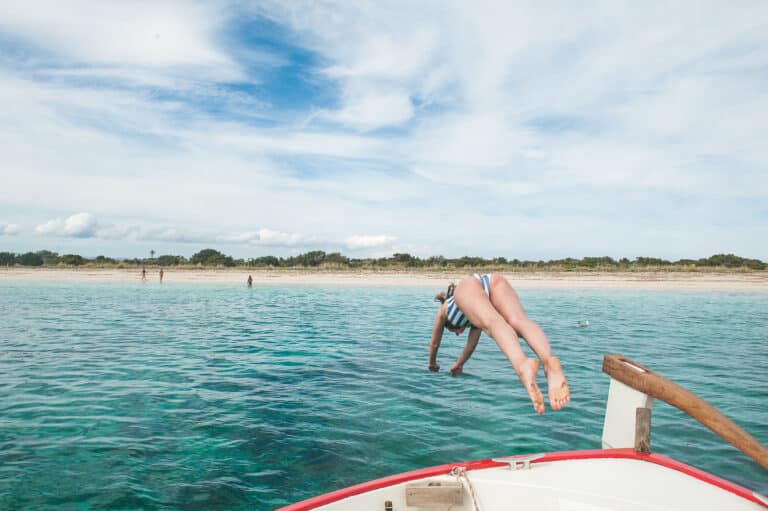 A joyful full-day tour participant diving into the crystal-clear waters near Espalmador Island, reflecting the playful spirit of IATU BOATS sailing excursions.