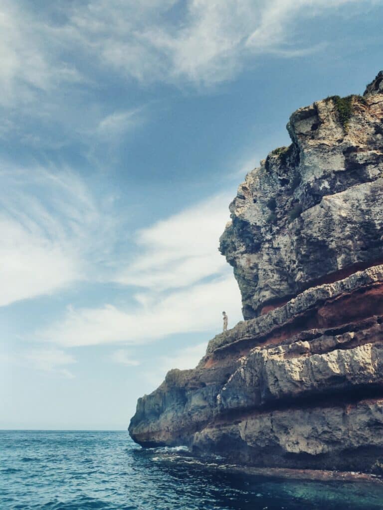 Adventurer standing atop the rugged cliff formations of Punta Prima, contemplating the vast sea on a full-day tour, a moment of connection with Formentera's wild beauty.