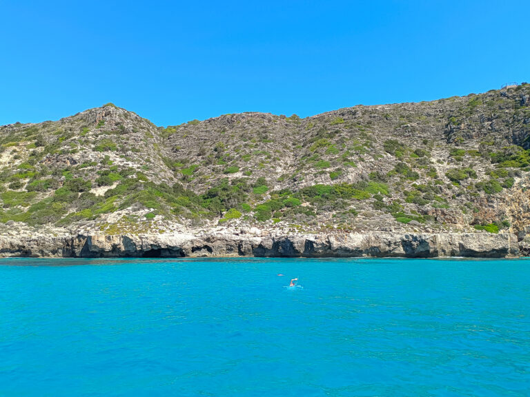 Discover the authentic essence of Formentera. A couple swimming alone in crystal blue waters in front of a cliff in Formentera with in a summer sunny day. Half day Tour